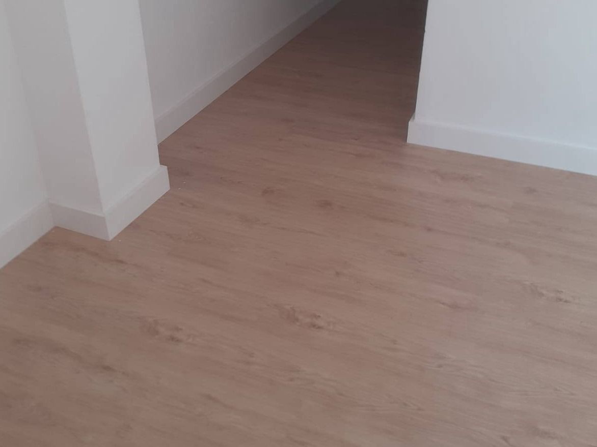 Estancia vacía con suelo de tarima de tono claro y rodapié blanco recién instalados
