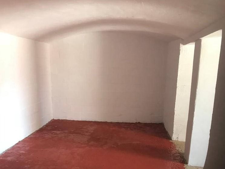 Sótano abovedado reformado como bodega, con paredes blancas y suelo rojo